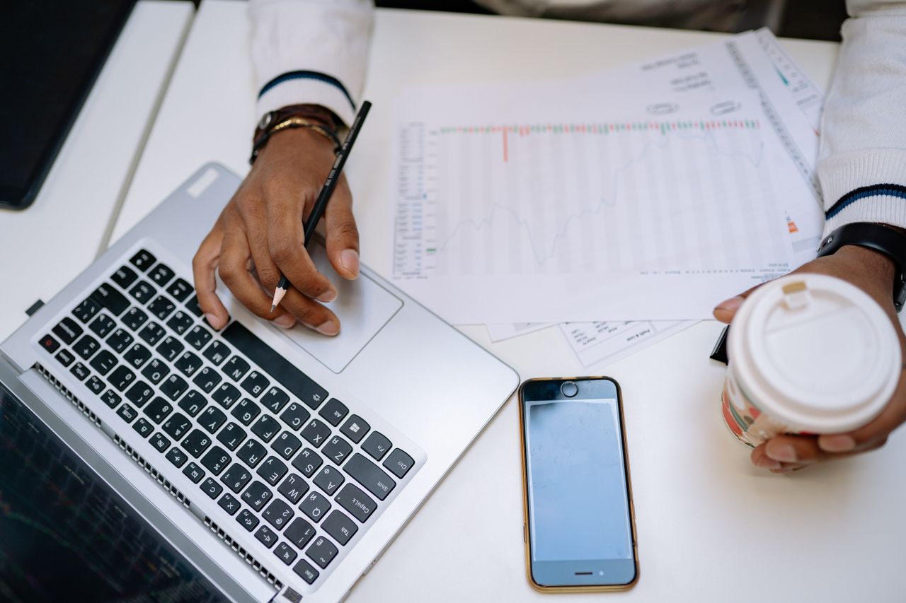 Services A businessman holding coffee and using a laptop at a desk with charts and a smartphone.